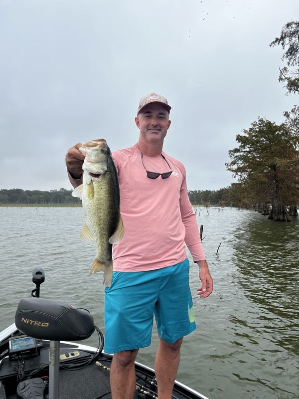 Jeremiah King on the front deck of his bass boat holding a largemouth bass, cypress trees behind