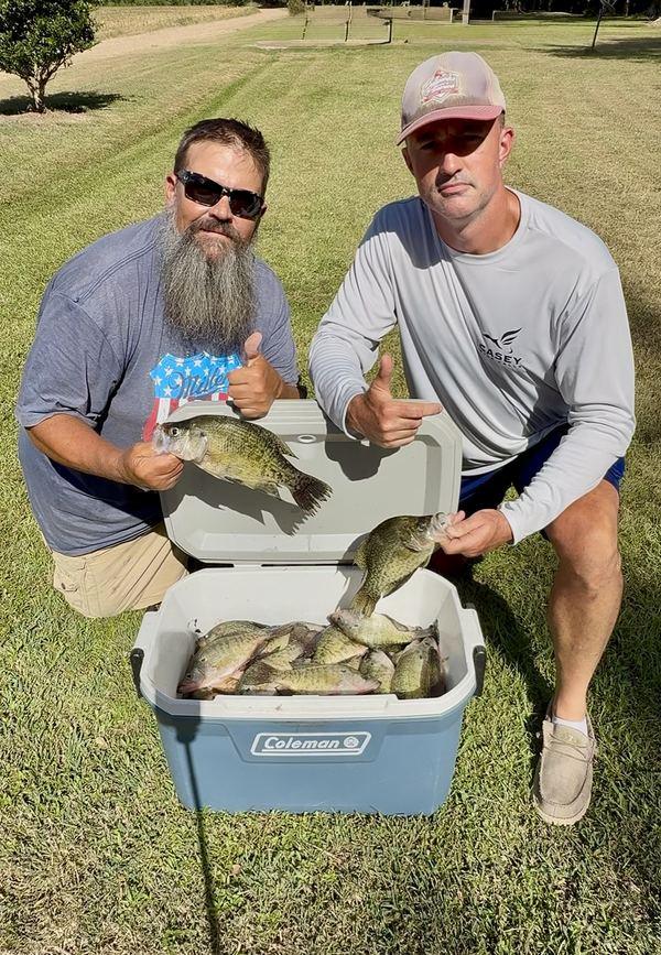 Jeremiah and a friend kneeling by a cooler of crappie, each holding one up